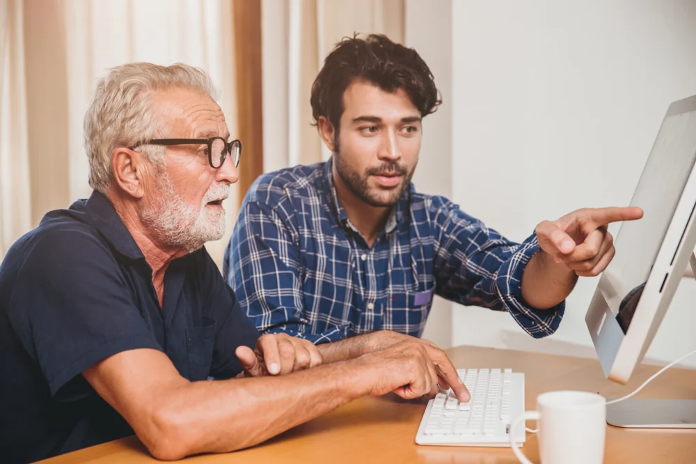 Technician helping a senior with computer setup during an in-home tech support visit