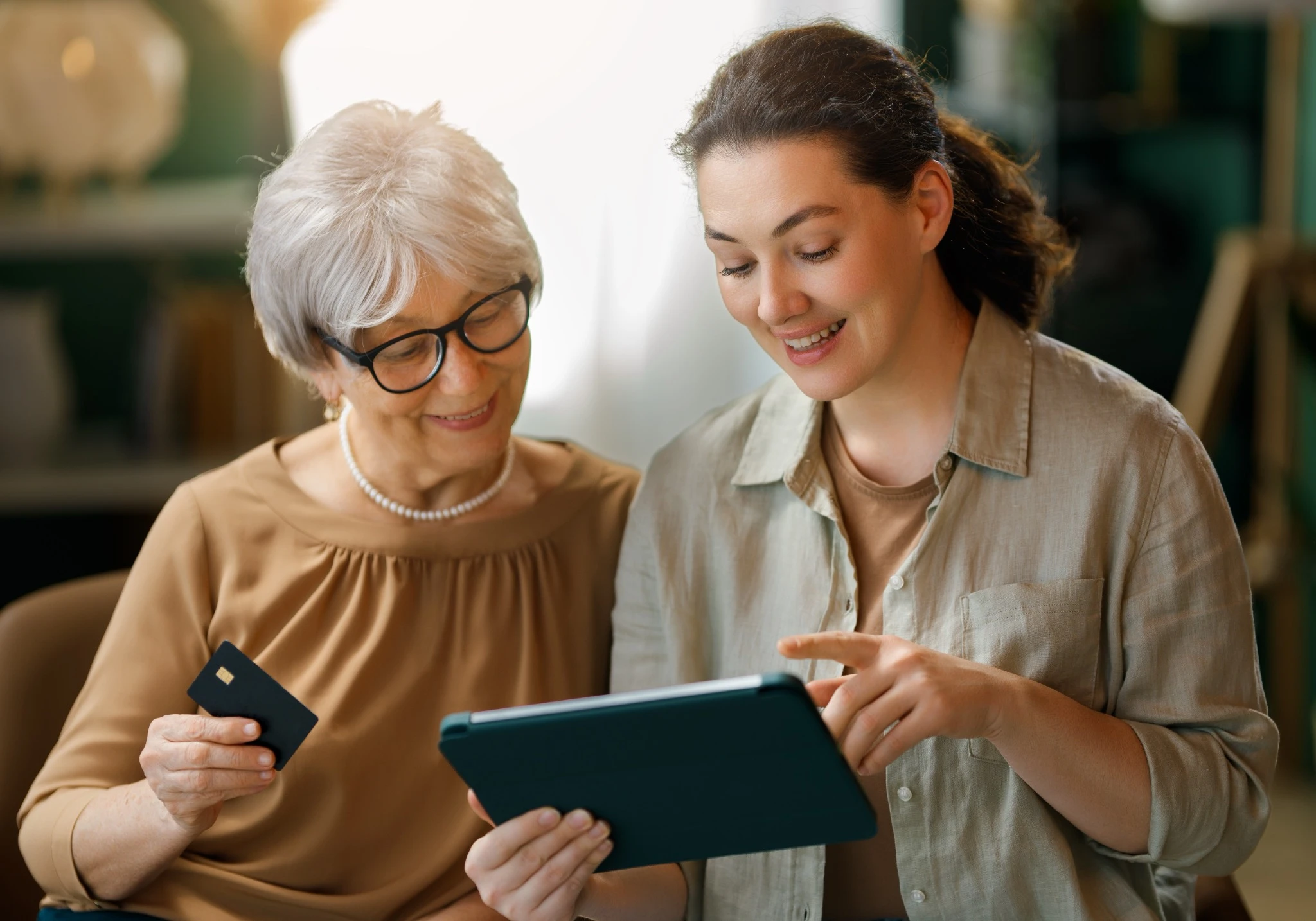 Senior customer receiving friendly technology assistance at home while reviewing service options and pricing on a tablet.