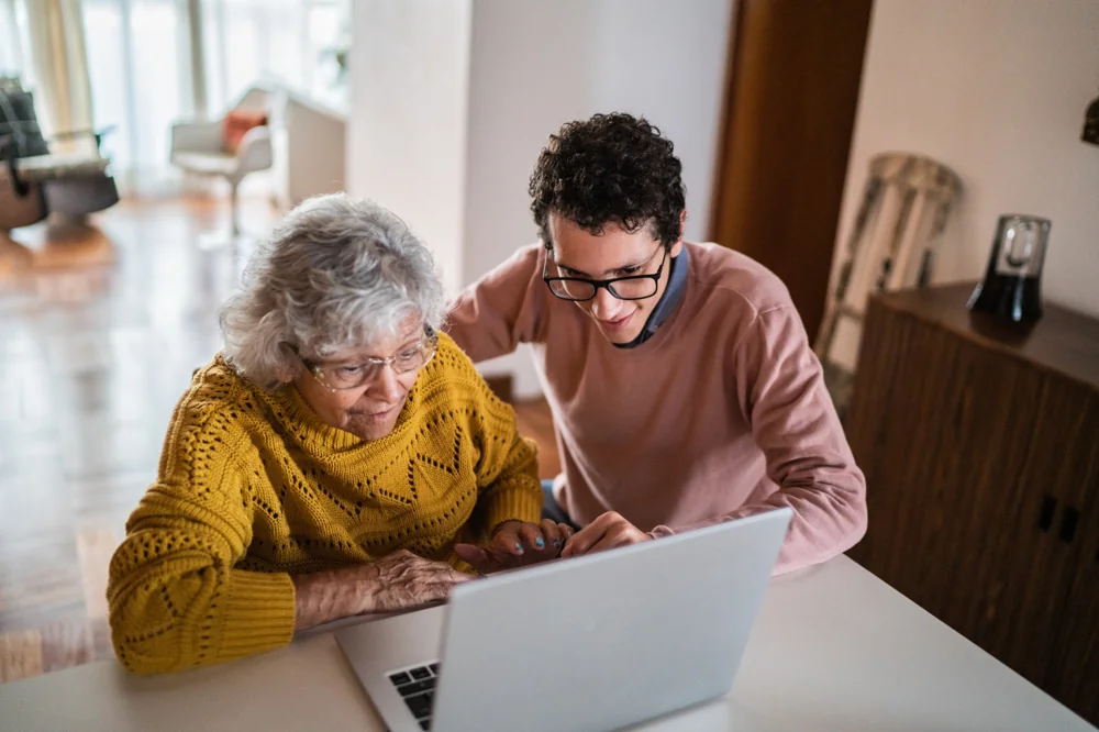 Technician patiently helping a senior use a laptop at home with step-by-step guidance